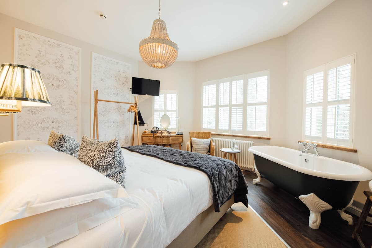 A bedroom with a large bed, a black bathtub, and a desk with a chair.