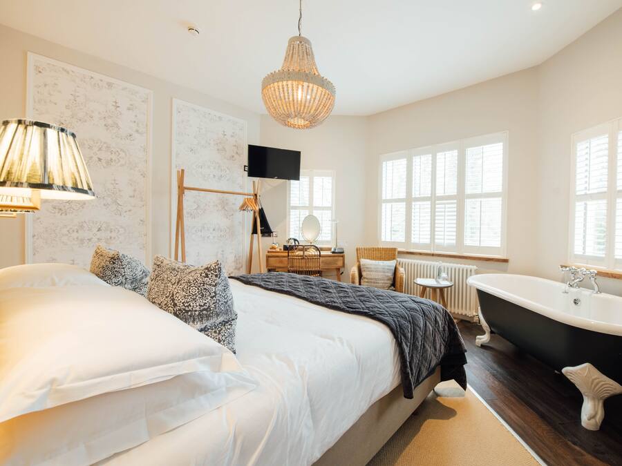 A bedroom with a large bed, a black bathtub, and a desk with a chair.