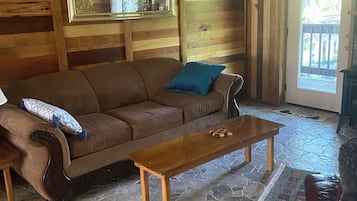 A wooden interior with a stone floor, a brown sofa, a wooden coffee table, and a ceiling fan.