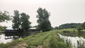 A riverside building with a dock, surrounded by lush greenery and a calm river. - Country Home with Pond and Great Outdoor Space (Nashport)
