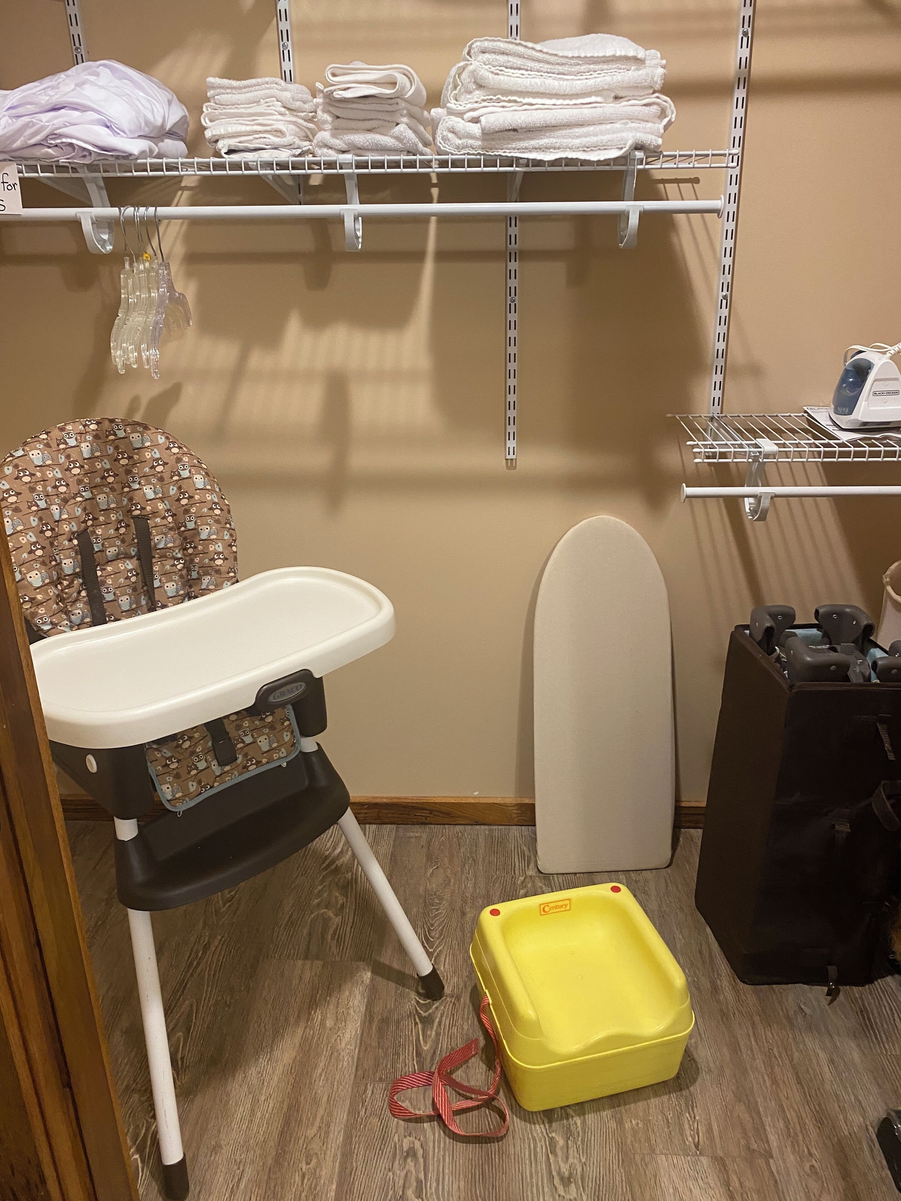 Un espace dédié à la lessive, avec une étagère où sont pliées les serviettes, un espace pour changer les bébés, un tableau à repasser et un panier à linge jaune.