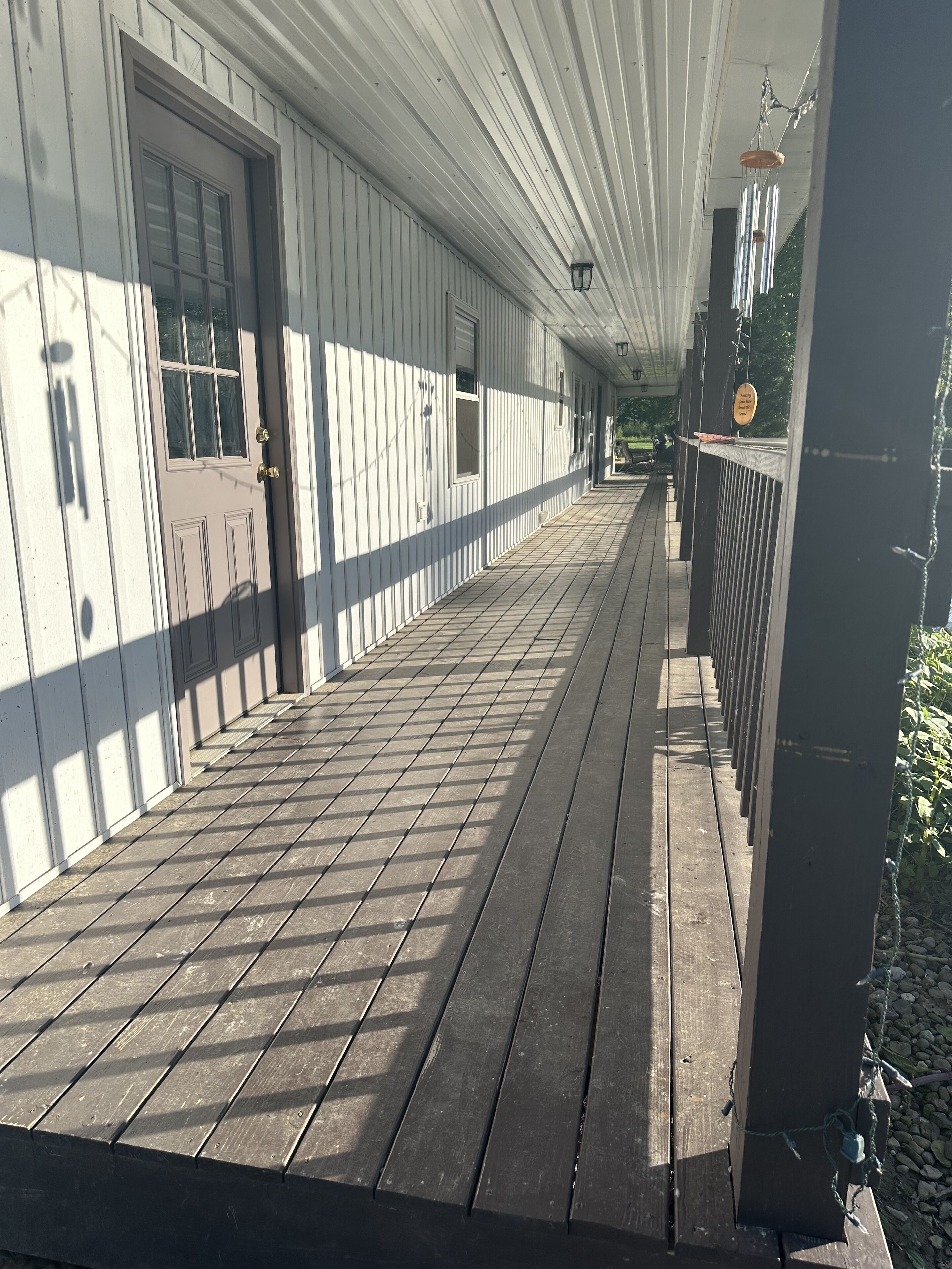 En overdækket træterrasse med gelænder, dør og en hængende lygte.