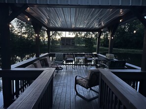 A covered outdoor deck with wooden furniture and a view of a lake. - Country Home with Pond and Great Outdoor Space (Nashport)