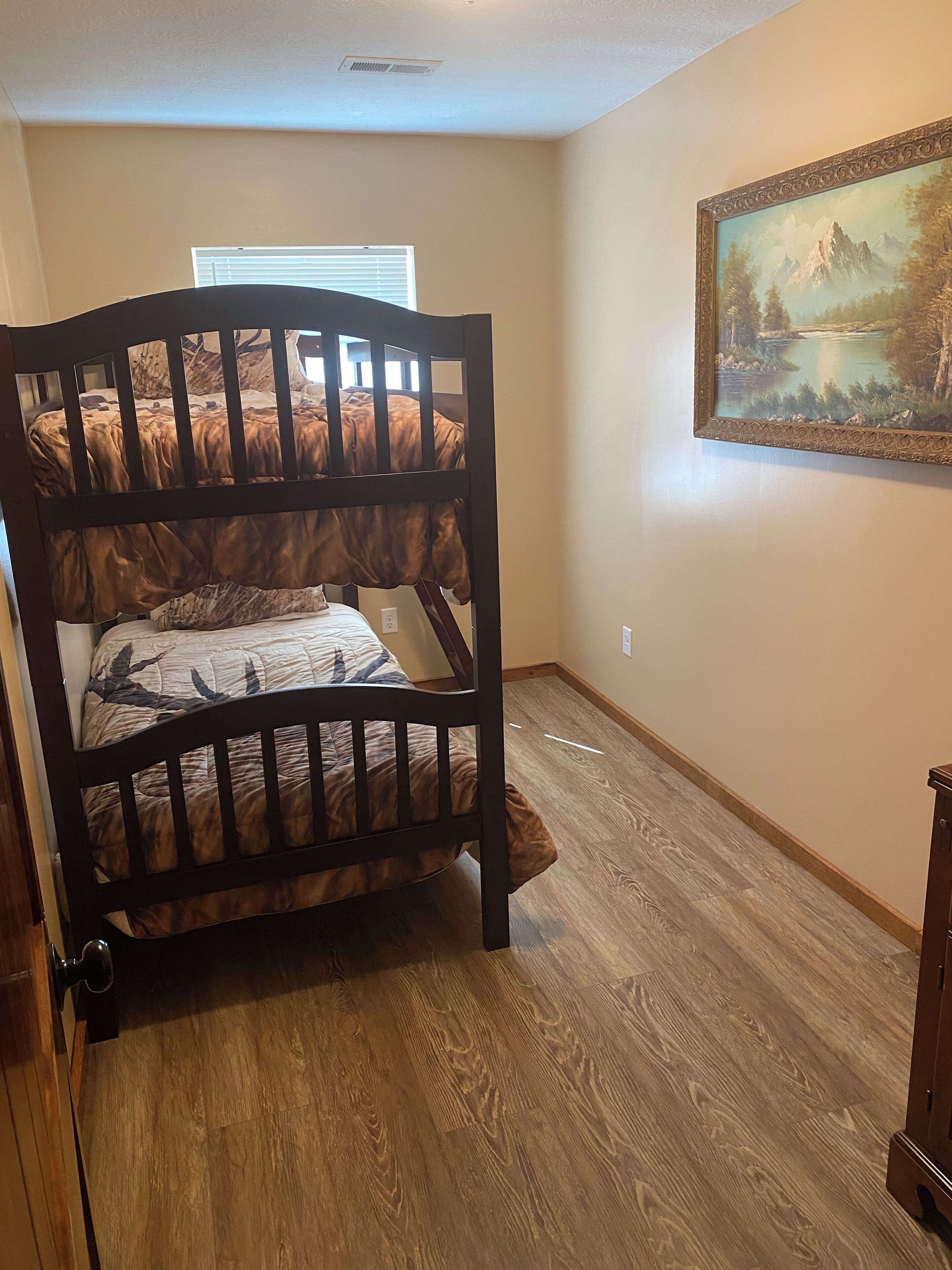 Una cama litera con un edredón estampado, un cuadro en la pared y suelo de madera.