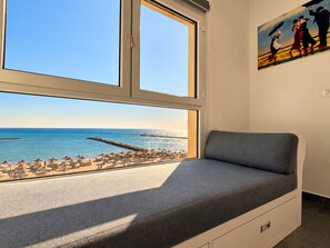 Habitación con un amplio ventanal con vistas a la playa, un sofá gris y un cuadro en la pared.