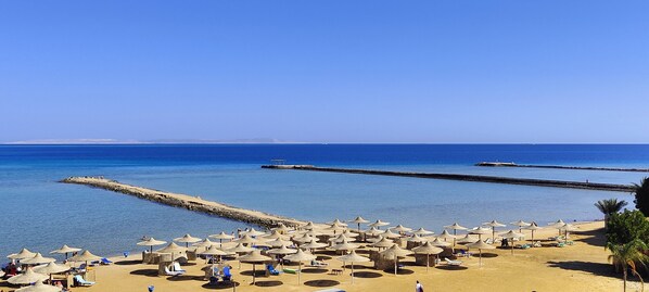 A beach with numerous sun umbrellas and lounge chairs, a clear blue sky, and calm sea.