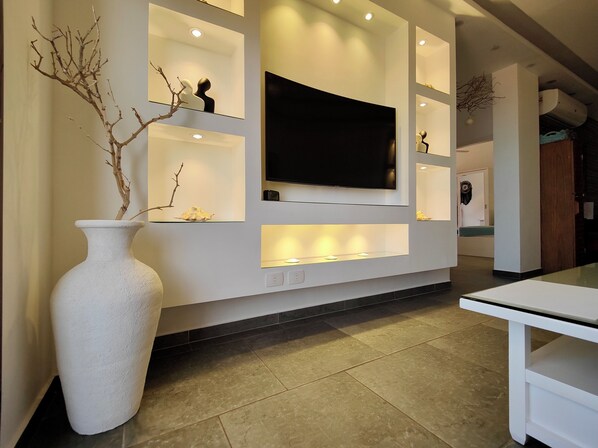 A modern interior with a large flat-screen TV mounted on a wall, a white vase with branches, and recessed lighting.