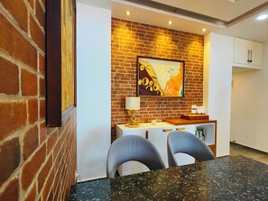 A dining area with a brick wall, a framed artwork, a table with chairs, and a white cabinet.