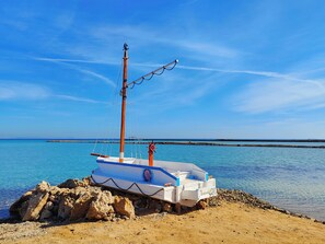 A small boat with a mast and rigging, docked on a rocky shore by the sea.