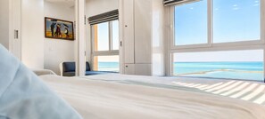 Habitación de hotel con cama, escritorio y un amplio ventanal con vistas al mar.