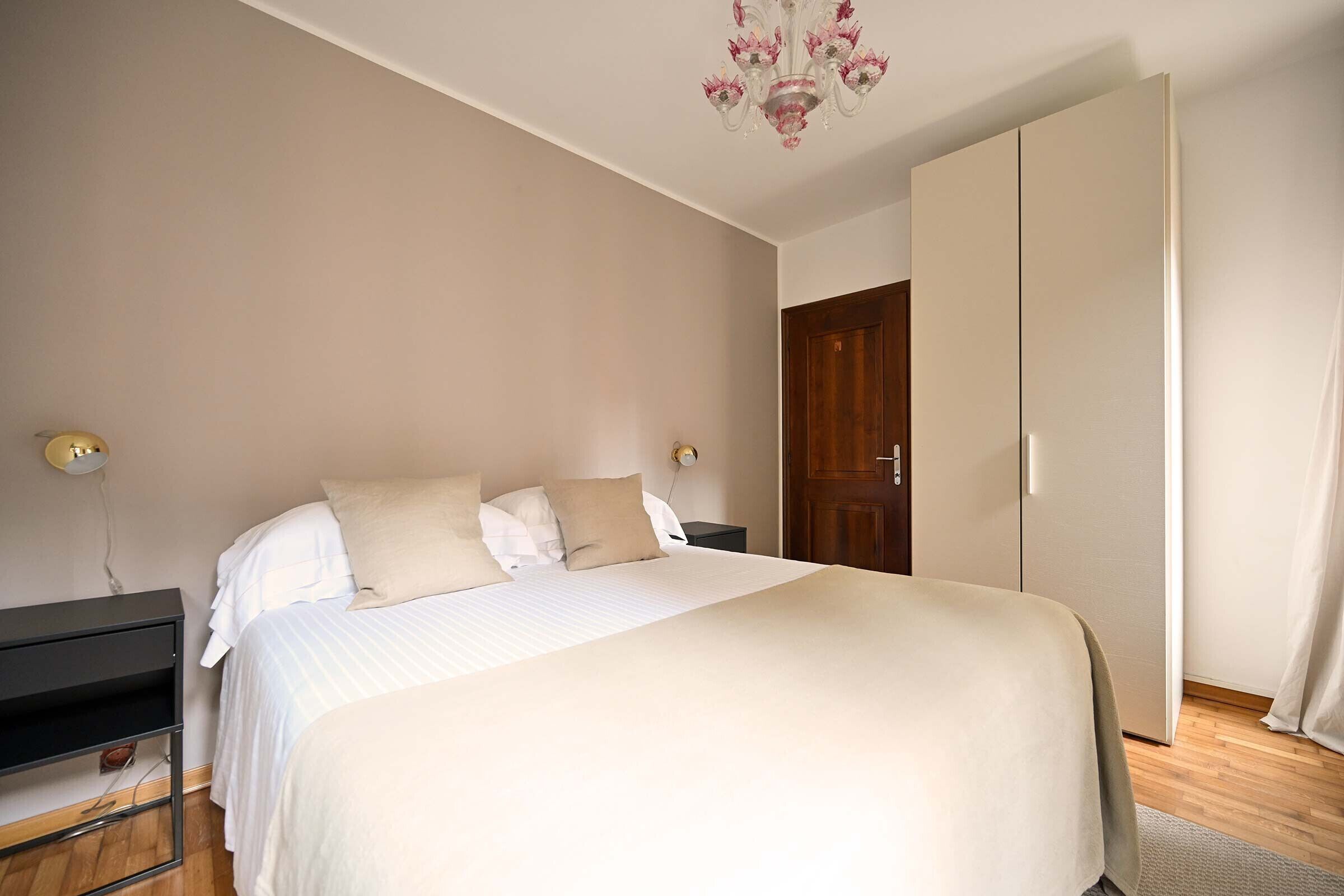 Une chambre à coucher avec un lit, des tables de chevet, une armoire et un lustre.