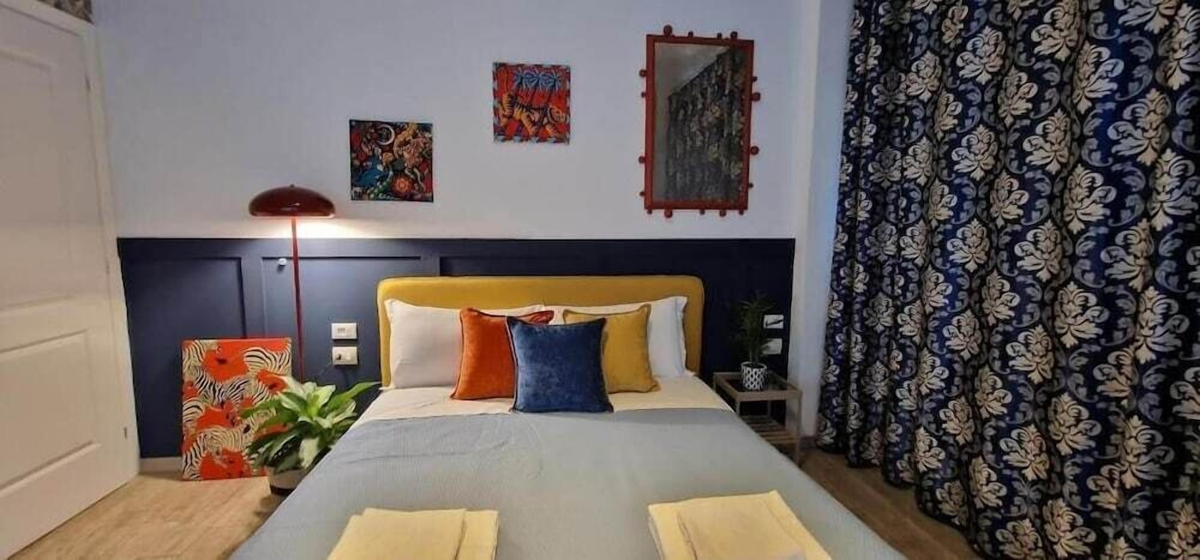 A neatly made bed with pillows, a bedside table with a lamp, and a wall with three artworks.