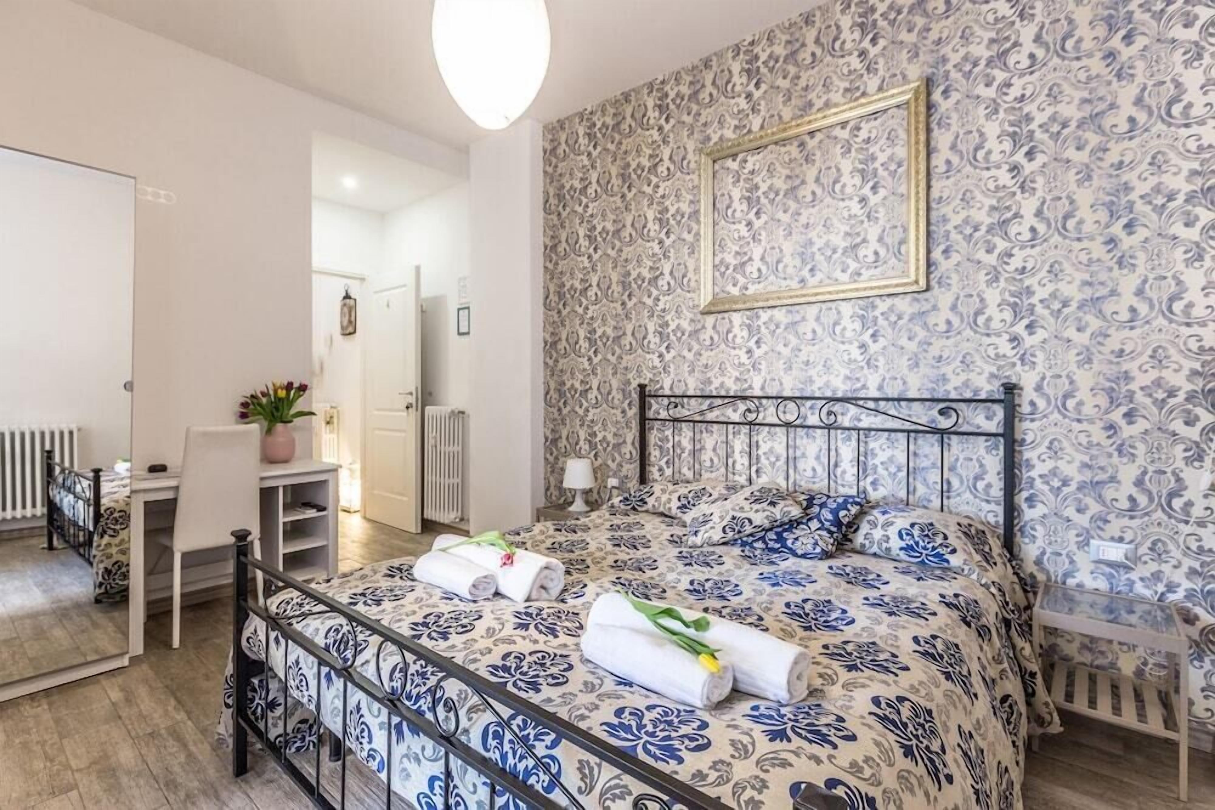 A bedroom with a bed, a desk, and a chair. There is a radiator and a potted plant.