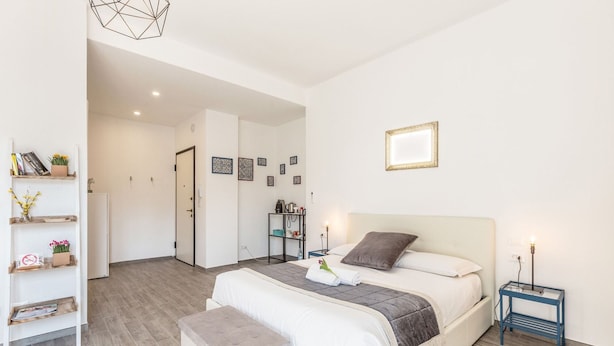 A modern bedroom with a large bed, bedside tables, a bench, and a wall-mounted light fixture. - Central City Inn (Bologna)