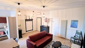 A modern living room with a red sofa, a dining table, and a kitchen area with white cabinets. - Central City Inn (Bologna)