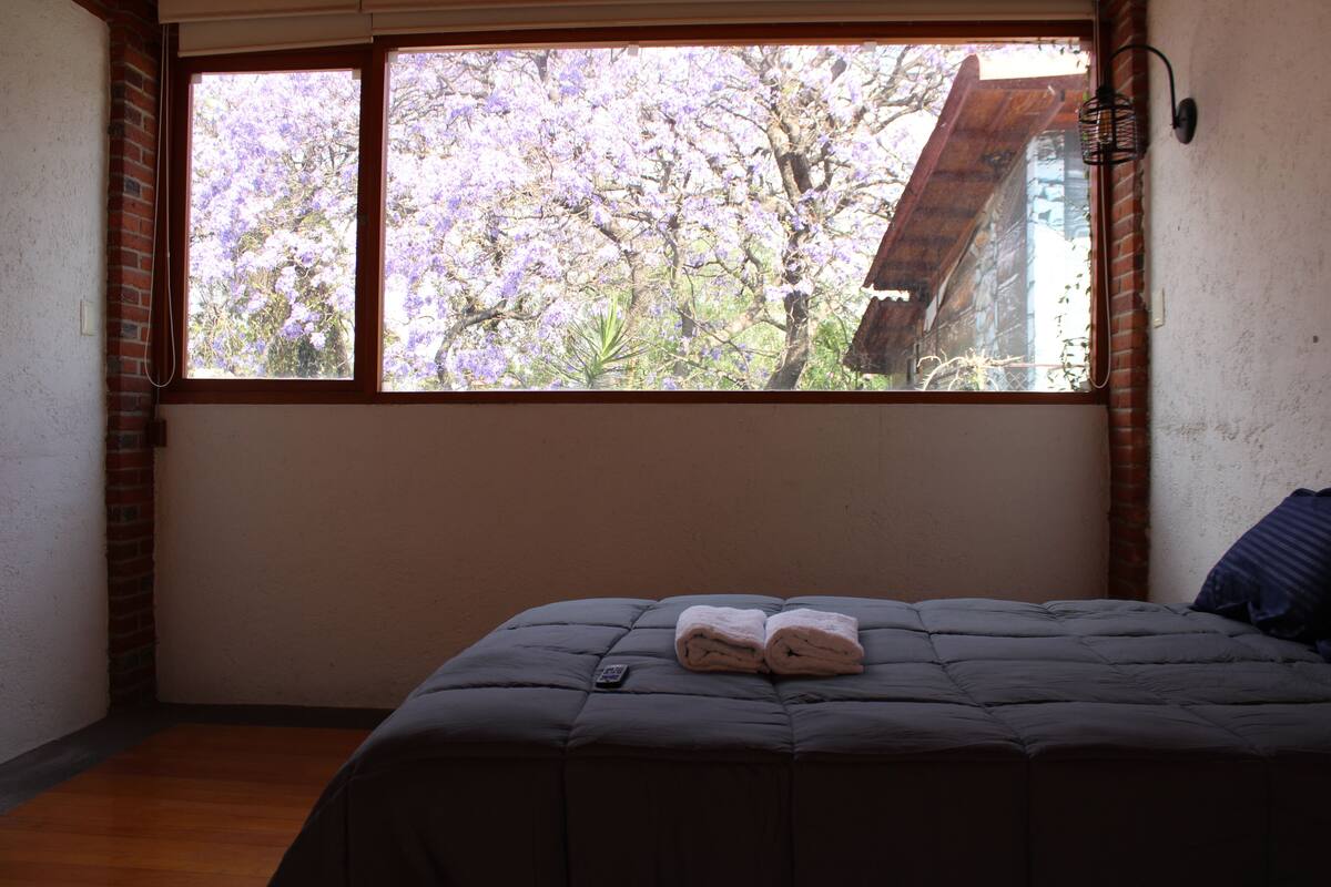 A bedroom with a large window, a bed, and a remote control on the bed.
