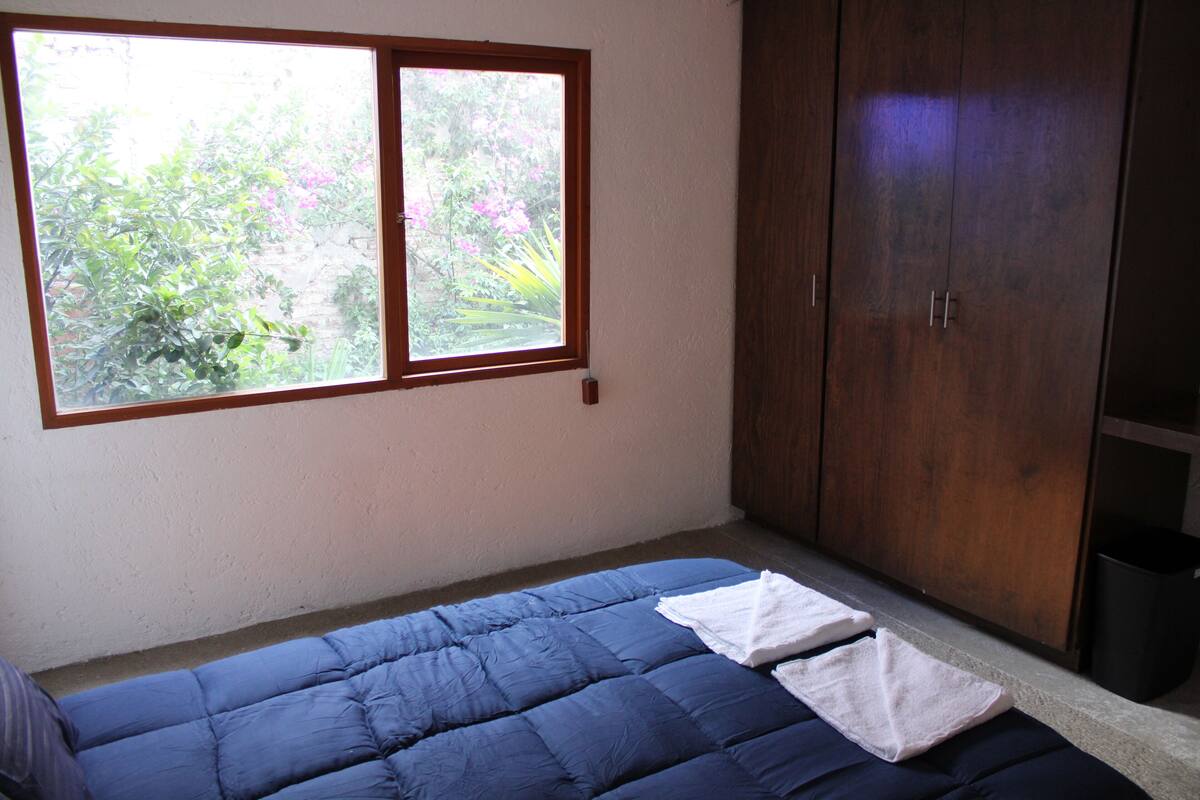 A bedroom with a single bed, a window with a view of greenery, and a wardrobe.