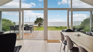 A spacious room with large windows offering a view of wind turbines and a body of water. - Cozy home in Ebeltoft (Ebeltoft)
