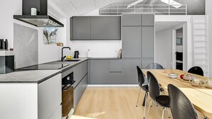 A modern kitchen with grey cabinets, a black countertop, and a wooden dining table with black chairs. - Cozy home in Ebeltoft (Ebeltoft)