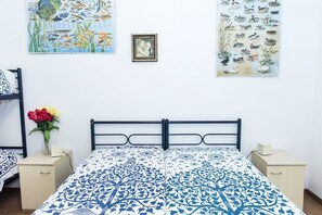 Une chambre à coucher comprenant un lit, deux tables de chevet, une commode, un mur orné de deux tableaux encadrés et un vase avec des fleurs.