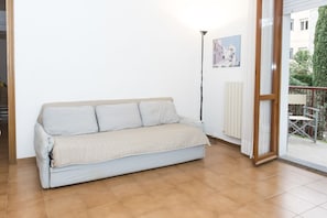 Une pièce avec un canapé, une lampe, un tableau et une vue sur l’extérieur, visible à travers une porte vitrée.