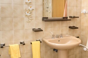 Un baño con baldosas color beige, un lavamanos, un espejo y toalleros.