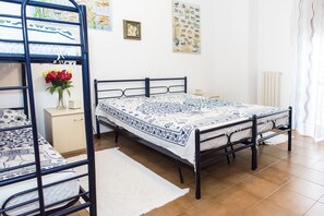 Una habitación con una cama litera, una cama individual, una mesita de noche, un florero con flores y decoración en la pared.