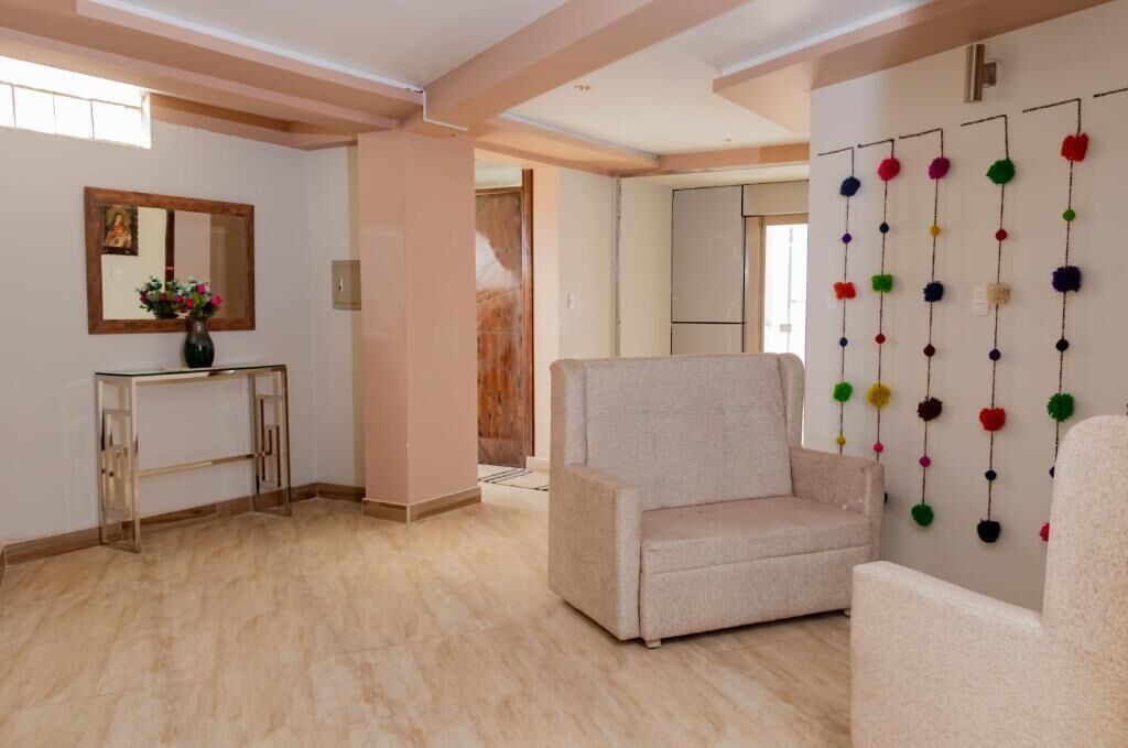 Una sala de estar con un sofá color beige, una consola de vidrio con un florero y una pared decorada con pompones de colores.
