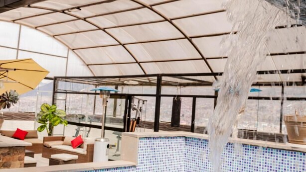 A covered pool area with a waterfall feature, seating, and a view of the outdoors. - Samay Business Hotel  (Cusco)
