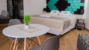 A hotel room with a bed, a round dining table, chairs, a potted plant, and a wall with a geometric design. - Samay Business Hotel  (Cusco)