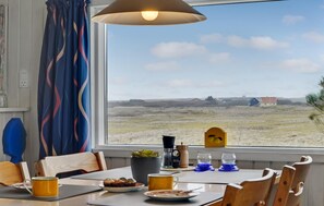 Un comedor con una mesa dispuesta para dos personas, una ventana con vistas al paisaje rural y una lámpara sobre la mesa.