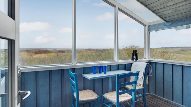 A covered outdoor seating area with a table and chairs, a view of the countryside, and a pair of binoculars on the table.