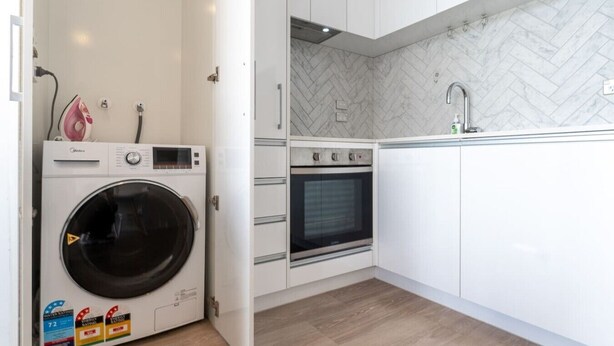 A compact kitchen with a built-in washing machine, oven, and a herringbone-patterned backsplash. - City Escape 1-Bedroom Studio with Pool in CBD (Auckland)