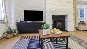 A living room with a fireplace, a flat-screen TV, a dining table with a plate of cake, and a potted plant. - Cornhill Courtyard (Porthmadog)