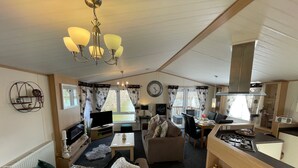 A cozy living room with a sofa, coffee table, and TV, connected to a dining area with chairs and a kitchen with a stove.