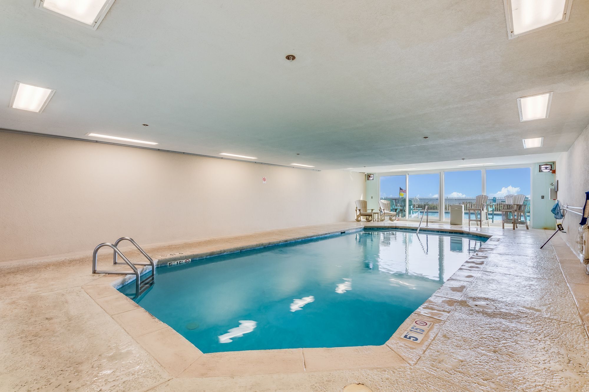 An indoor swimming pool with clear blue water, surrounded by walls and a ceiling with recessed lighting.