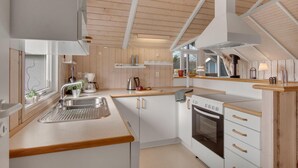 Ett modernt kök med trädetaljer, en inbyggd ugn och ett fönster med utsikt över ett hus.