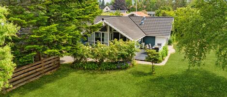 A house with a sloped roof, surrounded by a well-maintained lawn and dense greenery.