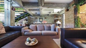 Una sala moderna con un conjunto de sofás, una mesa de centro con objetos decorativos, paredes de ladrillo visto y una escalera con plantas.
