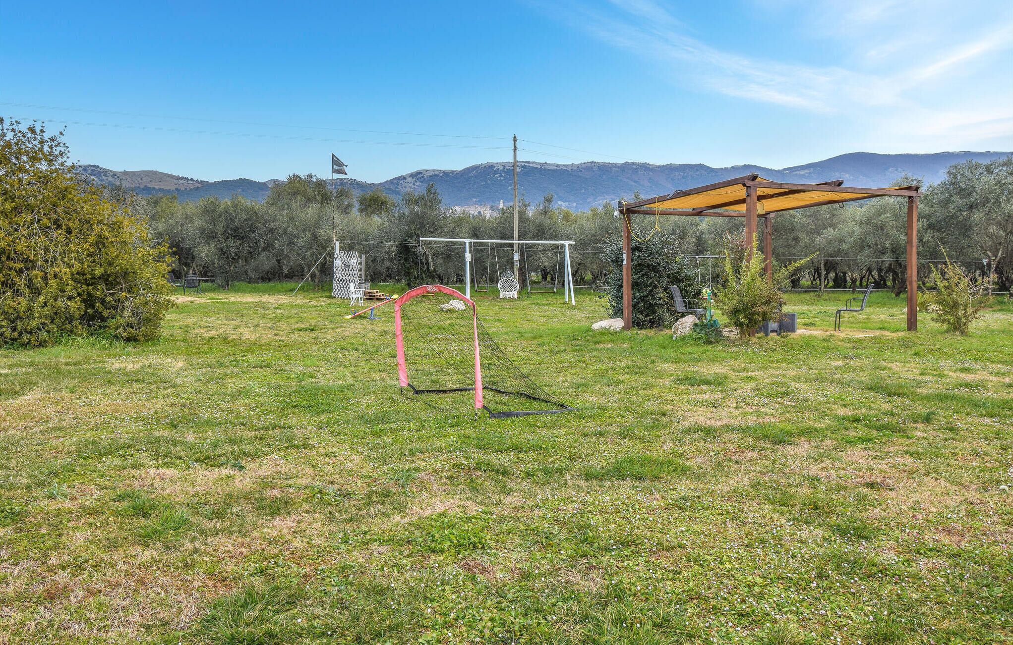 A grassy outdoor area with a wooden pergola, a soccer goal, and a swing set.