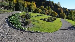 Un jardin aménagé avec un chemin de gravier, des haies soigneusement taillées et une variété d’arbres aux couleurs automnales.