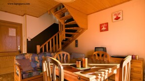 Une pièce chaleureuse avec un escalier en bois, un canapé, une table à manger et des chaises.