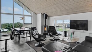 Una sala de estar moderna con chimenea, asientos cómodos, un comedor y ventanas amplias que ofrecen vistas al exterior.