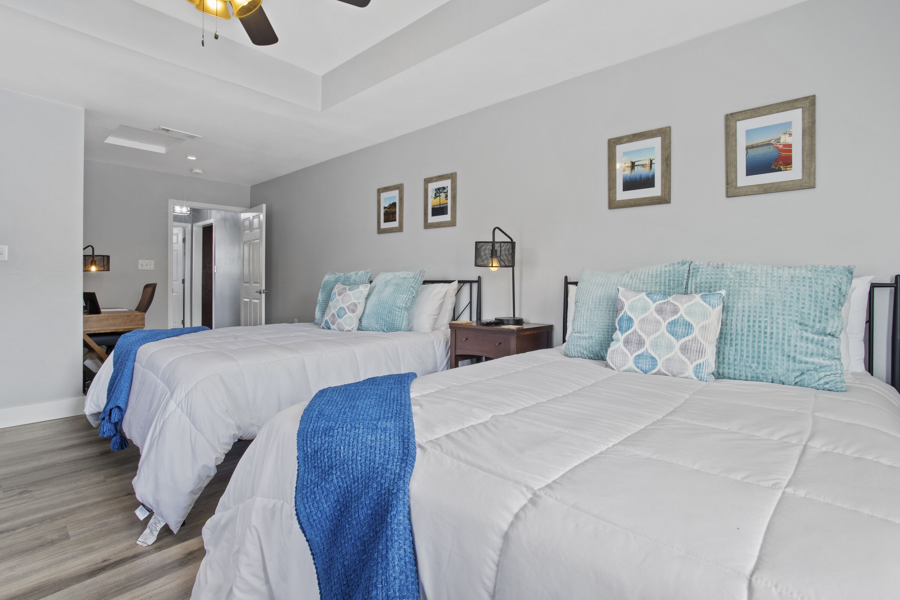 A hotel room with two beds, a desk, and a chair. There are framed pictures on the wall.