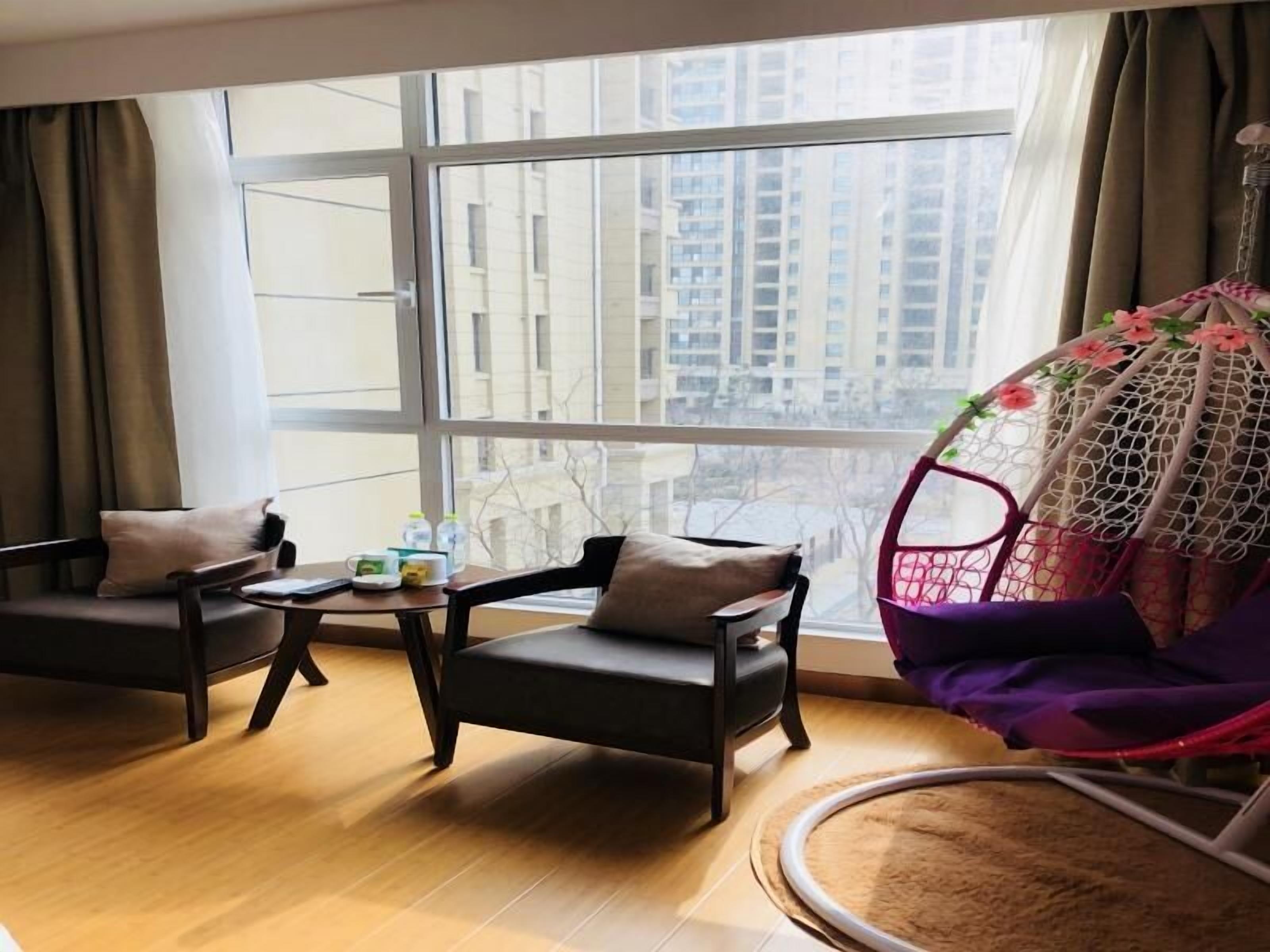 A modern living room with a large window, two sofas, a small table, and a hanging chair with a floral design.