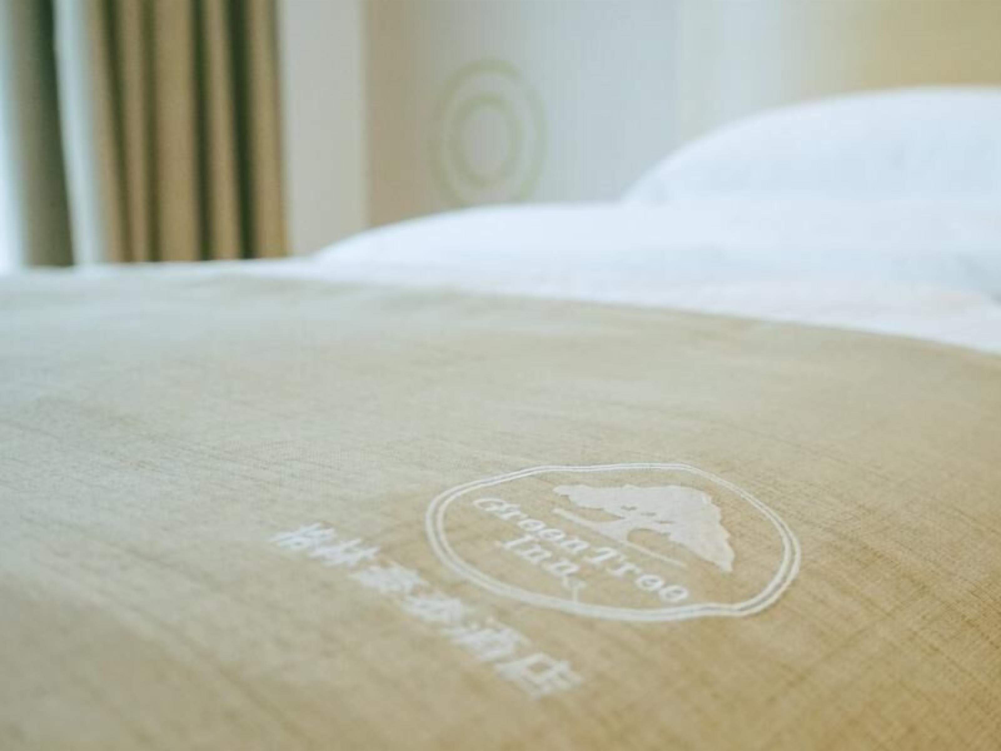 A bed with a white pillow and a beige bedspread featuring a circular logo with text.