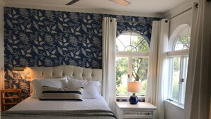 Une chambre à coucher avec un lit, une table de chevet, une lampe, une fenêtre avec des rideaux et un mur à motifs.