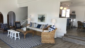Un salon spacieux avec un canapé, une table basse et des fauteuils. Un escalier mène à un autre niveau.