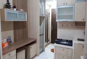 A compact kitchen with a built-in stove, a refrigerator, and a microwave. There is a small countertop with a few items on it, and a cabinet above the counter.