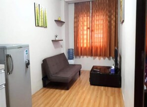 A compact living space with a grey sofa, a small table, a water dispenser, and a refrigerator. - Apartmen City Park by GC Realty by Zuzu (Jakarta)